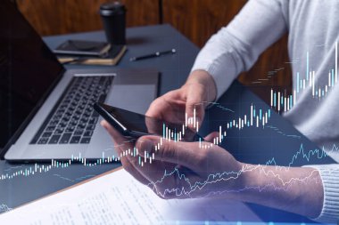 Elinde akıllı bir telefon tutan tüccar doğru yatırım çözümlerine ulaşmak için borsayı araştırıyor. İnternet ticareti ve zenginlik yönetimi kavramı. Hologram Forex grafiği yakın çekim üzerine.