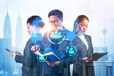 İş amaçlarına ulaşmak için sosyal medya pazarlama stratejisi üzerinde çalışan bir grup SMM uzmanı. Kuala Lumpur arkaplanı üzerinde hologram simgeleri.
