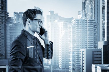 Takım elbiseli, gözlüklü, telefonla konuşan ve Bangkok 'un manzarasına bakan başarılı yakışıklı girişimci. Sorun çözme danışmanlığı kavramı. Şehir merkezi manzarası. Çift pozlama.