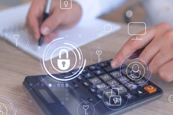Bir iş adamı, hesap makinesi kullanarak siber güvenlik korumasında risk olasılığını hesaplıyor. Çalışma masasının üzerine asma kilit hologramı simgeleri. Resmi giysi.