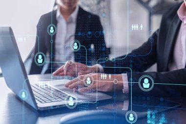 İki İK uzmanı, uluslararası danışmanlık şirketindeki stajyerlik programını hızlandırmak için dizüstü bilgisayar kullanarak işe alım pazarını analiz ediyor. Sosyal ağ hologram simgeleri.