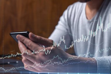 Elinde akıllı bir telefon tutan tüccar doğru yatırım çözümlerine ulaşmak için borsayı araştırıyor. İnternet ticareti ve zenginlik yönetimi kavramı. Hologram Forex grafiği yakın çekim üzerine.