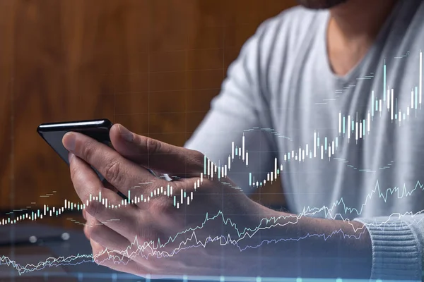Elinde akıllı bir telefon tutan tüccar doğru yatırım çözümlerine ulaşmak için borsayı araştırıyor. İnternet ticareti ve zenginlik yönetimi kavramı. Hologram Forex grafiği yakın çekim üzerine.