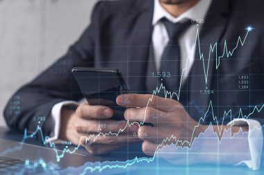 Elinde akıllı bir telefon tutan tüccar doğru yatırım çözümlerine ulaşmak için borsayı araştırıyor. İnternet ticareti ve zenginlik yönetimi kavramı. Hologram Forex grafiği yakın çekim üzerine.