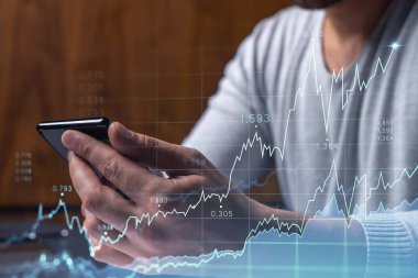 Elinde akıllı bir telefon tutan tüccar doğru yatırım çözümlerine ulaşmak için borsayı araştırıyor. İnternet ticareti ve zenginlik yönetimi kavramı. Hologram Forex grafiği yakın çekim üzerine.