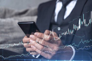 Elinde akıllı bir telefon tutan tüccar doğru yatırım çözümlerine ulaşmak için borsayı araştırıyor. İnternet ticareti ve zenginlik yönetimi kavramı. Hologram Forex grafiği yakın çekim üzerine.