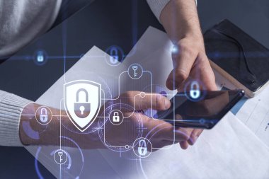Bir programcı, bir siber güvenliği hacker saldırılarından korumak ve müşterilerinin gizli verilerini kaydetmek için akıllı telefonuyla internete giriyor. Yazan ellerin üzerine asma kilit hologramı simgeleri.