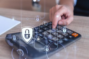 Bir iş kadını, hesap makinesi kullanarak siber güvenlik korumasında risk olasılığını hesaplıyor. Çalışma masasının üzerine asma kilit hologramı simgeleri. Resmi giysi.