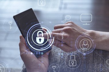 Bir programcı, bir siber güvenliği hacker saldırılarından korumak ve müşterilerinin gizli verilerini kaydetmek için akıllı telefonuyla internete giriyor. Yazan ellerin üzerine asma kilit hologramı simgeleri.