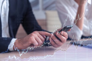 İki tüccar, dizüstü bilgisayar ve telefon kullanarak borsa davranışlarını tahmin etmek için tarihi verileri araştırıyor. İnternet ticareti konsepti. Eski ve finansal hologram şeması. Tahmin ve planlama.