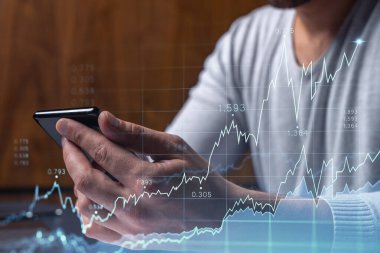 Elinde akıllı bir telefon tutan tüccar doğru yatırım çözümlerine ulaşmak için borsayı araştırıyor. İnternet ticareti ve zenginlik yönetimi kavramı. Hologram Forex grafiği yakın çekim üzerine.
