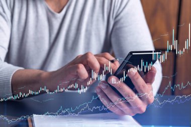Elinde akıllı bir telefon tutan tüccar doğru yatırım çözümlerine ulaşmak için borsayı araştırıyor. İnternet ticareti ve zenginlik yönetimi kavramı. Hologram Forex grafiği yakın çekim üzerine.