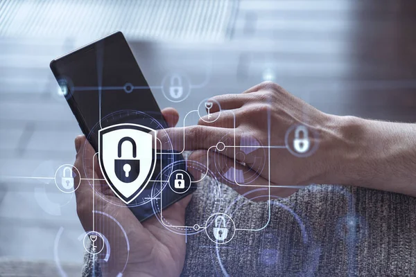 Bir programcı, bir siber güvenliği hacker saldırılarından korumak ve müşterilerinin gizli verilerini kaydetmek için akıllı telefonuyla internete giriyor. Yazan ellerin üzerine asma kilit hologramı simgeleri.