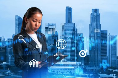 Takım elbiseli çekici Asyalı iş kadını uluslararası danışmanlık şirketinde araştırma ve geliştirme bölümünde başarılı olmak için not defterinden notlar okuyor. Singapur üzerinde hologram simgeleri.