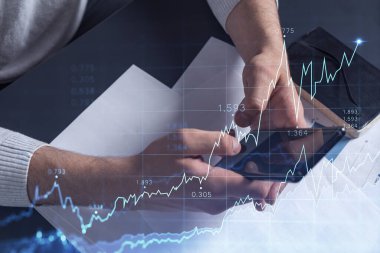 Elinde akıllı bir telefon tutan tüccar doğru yatırım çözümlerine ulaşmak için borsayı araştırıyor. İnternet ticareti ve zenginlik yönetimi kavramı. Hologram Forex grafiği yakın çekim üzerine.