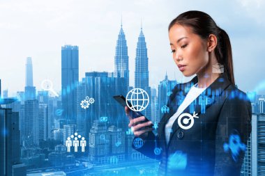 Akıllı telefonu araştırma ve geliştirme bölümündeki sorunları çözmek için modern bir araç olarak kullanan çekici Asyalı iş kadını. Kuala Lumpur üzerinde Fintech hologram simgeleri.