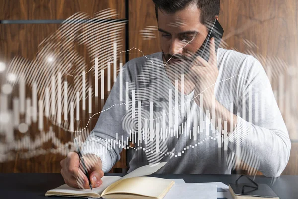 Handsome trader in casual long sleeve talking phone, taking notes at office workplace try to find the best capital market solution. Double exposure. Internet trading at FOREX exchange.
