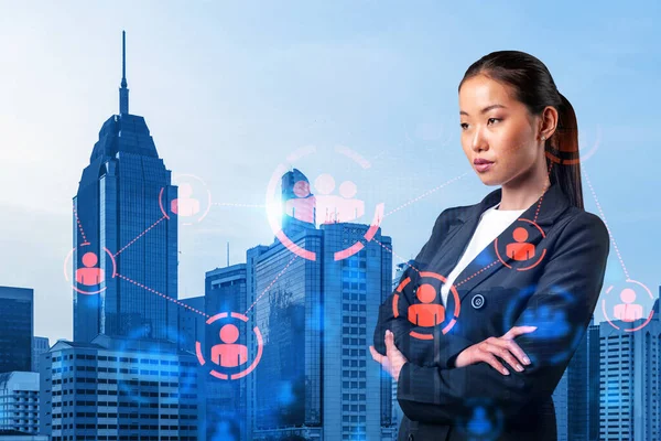 Attractive young Asian HR director at international company is thinking about recruitment of highly qualified specialists. Women in business concept. Social media hologram icons over Kuala Lumpur.