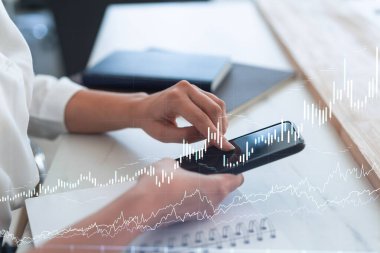 Elinde akıllı bir telefon tutan ve doğru yatırım çözümlerine ulaşmak için borsayı araştıran bir kadın tüccar. İnternet ticareti ve zenginlik yönetimi kavramı. Hologram Forex çizelgesi.