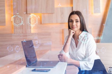 İş yerindeki beyaz tişörtlü çekici iş kadını iş hayatında yeni teknolojiler ima ederek gelişimi optimize etmek için dizüstü bilgisayarla çalışıyor. Ofis geçmişinde yüksek teknoloji hologramı