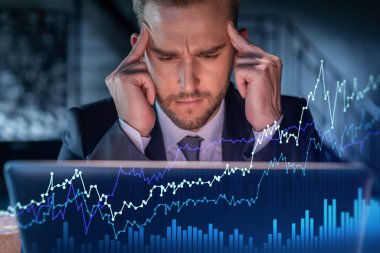 İş yerindeki takım elbiseli yakışıklı işadamı şirket finans fonundaki ticaret stratejisini optimize etmek için dizüstü bilgisayarla çalışıyor. Ofis arkaplanı üzerinde eski grafik hologramı