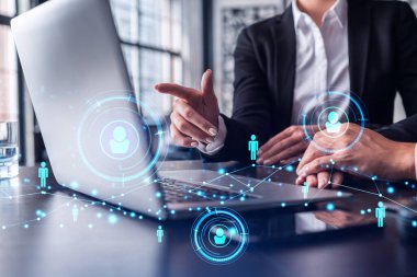 İki İK uzmanı, uluslararası danışmanlık şirketindeki stajyerlik programını hızlandırmak için dizüstü bilgisayar kullanarak işe alım pazarını inceliyor. Sosyal ağ hologram simgeleri.