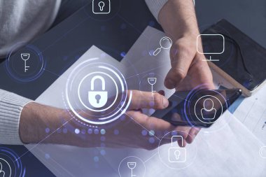 Bir programcı, bir siber güvenliği hacker saldırılarından korumak ve müşterilerinin gizli verilerini kaydetmek için akıllı telefonuyla internete giriyor. Yazan ellerin üzerine asma kilit hologramı simgeleri.