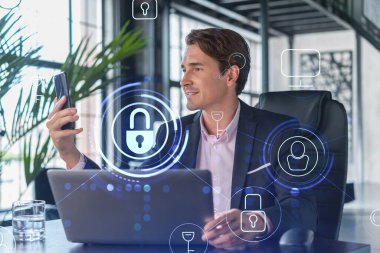 Takım elbiseli bir işadamı müşterileri korumak için siber güvenliği kontrol ediyor. IT hologramı modern panoramik ofis arkaplanı üzerine simgeleri kilitledi.