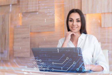 İş yerindeki beyaz tişörtlü çekici iş kadını iş hayatında yeni teknolojiler ima ederek gelişimi optimize etmek için dizüstü bilgisayarla çalışıyor. Ofis geçmişinde yüksek teknoloji hologramı