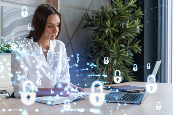 Attraktiv forretningskvinde i hvid skjorte på arbejdspladsen arbejder med laptop til at forsvare kundens cybersikkerhed. Begrebet kundeinformationsbeskyttelse. Hængelås hologram over kontorbaggrund. - Stock-foto