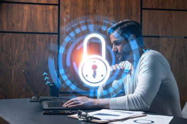 Ciddi bir Kafkasyalı programcı, verileri korumak için yeni bir güvenlik sistemi geliştirmek için dizüstü bilgisayar kullanıyor. Çifte maruziyet. IT hologram simgesini kilitle.