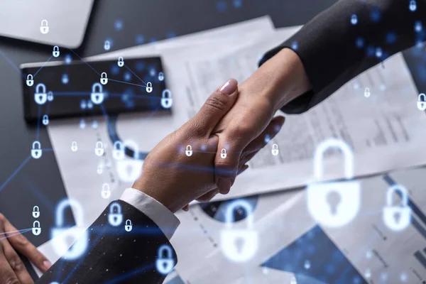 国際企業のサイバーセキュリティを保護するために契約に入る2人のビジネス女性の握手。ドキュメントとテーブルの上の南京錠ホログラムアイコン. — ストック写真