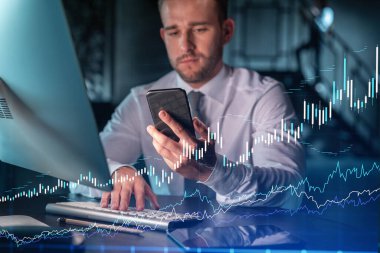 Sıradan giyinen iş adamı, kurumsal finans fonundaki ticaret stratejisini optimize etmek için akıllı telefon kullanıyor. Eski çizelge hologramı modern ofis arkaplanı üzerinde gece vakti