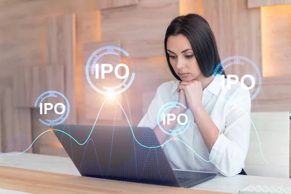 Привлекательная деловая женщина в белой рубашке на рабочем месте, работающая с ноутбуком для оптимизации стратегии IPO в корпоративном фонде. Голограмма финансового графика на фоне офиса — стоковое фото