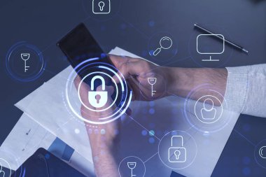 Bir programcı, bir siber güvenliği hacker saldırılarından korumak ve müşterilerinin gizli verilerini kaydetmek için akıllı telefonuyla internete giriyor. Yazan ellerin üzerine asma kilit hologramı simgeleri.