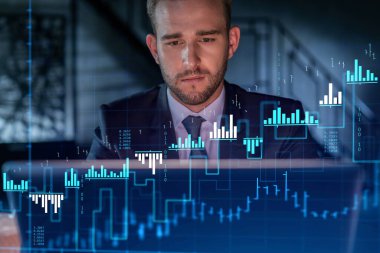 İş yerindeki takım elbiseli yakışıklı işadamı şirket finans fonundaki ticaret stratejisini optimize etmek için dizüstü bilgisayarla çalışıyor. Ofis arkaplanı üzerinde eski grafik hologramı
