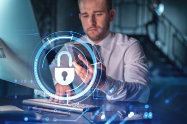 Sıradan giyinen bir iş adamı müşterileri gizli bilgilerini korumak için akıllı telefon kullanarak siber güvenliği kontrol ediyor. IT hologramı, modern ofis arkaplanının üzerine gece vakti simge kilitler.