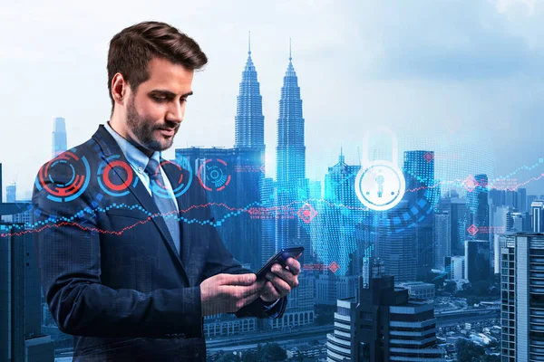 Un joven y guapo desarrollador de ciberseguridad caucásico explora nuevos enfoques para proteger la información confidencial de los clientes mediante el teléfono. Iconos de bloqueo de TI sobre fondo de la ciudad de Kuala Lumpur. — Foto de Stock