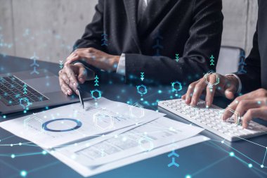 İki araştırma ve geliştirme uzmanı, işi geliştirmek için yazılım geliştirmeye yeni bir yaklaşım geliştirmek için proje üzerinde çalışıyor. Masanın üzerinde belgeyle birlikte teknolojik simgeler.