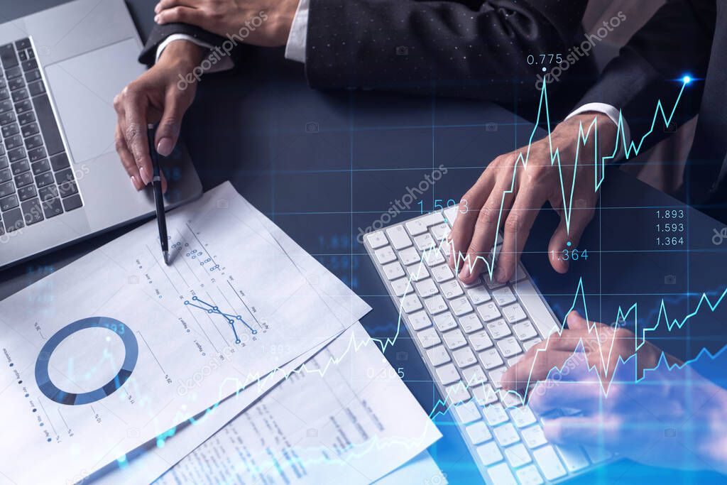 Two traders man and woman researching historic data to predict stock market behavior. Internet trading concept. Forex and financial hologram chart over the table with the documents