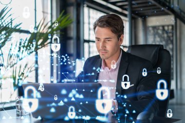 İş yerindeki yakışıklı iş adamı müşteri siber güvenliğini savunmak için dizüstü bilgisayarla çalışıyor. Müşterilerin bilgi koruması ve beyin fırtınası kavramı. Ofis arka planında asma kilit hologramı.