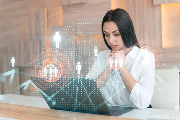 Attraktiv forretningskvinde i hvid skjorte på arbejdspladsen arbejder med laptop til at ansætte nye medarbejdere til international business rådgivning. HR, hologramikoner til sociale medier over kontorbaggrund - Stock-foto