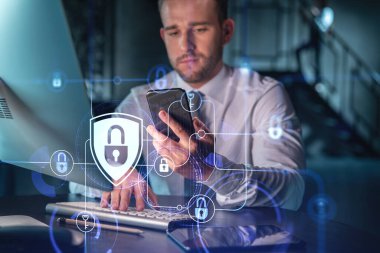 Sıradan giyinen bir iş adamı müşterileri gizli bilgilerini korumak için akıllı telefon kullanarak siber güvenliği kontrol ediyor. IT hologramı, modern ofis arkaplanının üzerine gece vakti simge kilitler.