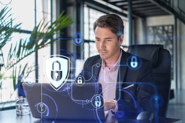 İş yerindeki yakışıklı iş adamı müşteri siber güvenliğini savunmak için dizüstü bilgisayarla çalışıyor. Müşterilerin bilgi koruması ve beyin fırtınası kavramı. Ofis arka planında asma kilit hologramı.