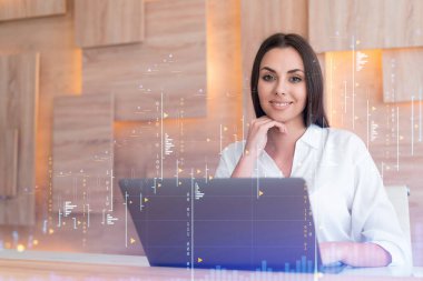 İş yerindeki beyaz gömlekli çekici iş kadını şirket finans fonunda ticaret stratejisini optimize etmek için dizüstü bilgisayarla çalışıyor. Ofis arkaplanı üzerinde eski grafik hologramı