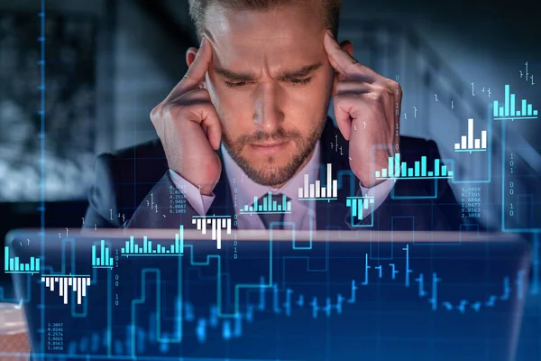İş yerindeki takım elbiseli yakışıklı işadamı şirket finans fonundaki ticaret stratejisini optimize etmek için dizüstü bilgisayarla çalışıyor. Ofis arkaplanı üzerinde eski grafik hologramı