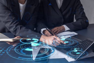 İki bilişim teknolojisi uzmanı iş hizmetlerini geliştirmek için yazılım geliştirmek üzere yeni bir yaklaşım geliştirme projesi üzerinde çalışıyor. Masanın üzerinde belgeyle birlikte teknolojik simgeler.