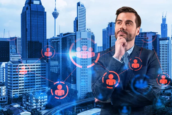 Handsome Caucasian HR director at international company is thinking about efficient strategy to recruit highly qualified specialists. Social media marketing hologram icons over Kuala Lumpur background