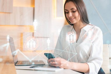 Beyaz gömlekli çekici bir iş kadını uluslararası iş danışmanlığı için yeni adayları kontrol etmek için akıllı telefon kullanıyor. Modern ofis geçmişi üzerinde HR ve sosyal medya simgeleri.
