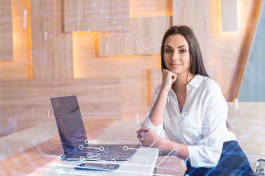 İş yerindeki beyaz tişörtlü çekici iş kadını iş hayatında yeni teknolojiler ima ederek gelişimi optimize etmek için dizüstü bilgisayarla çalışıyor. Ofis geçmişinde yüksek teknoloji hologramı